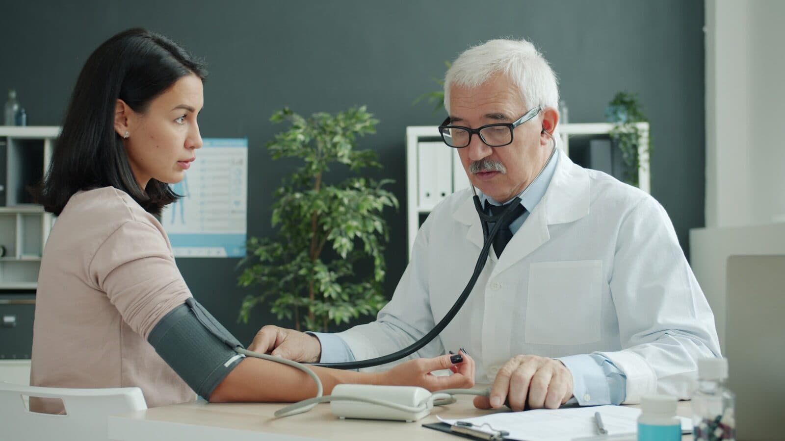 Doctor checks patient's blood pressure with stethoscope.
