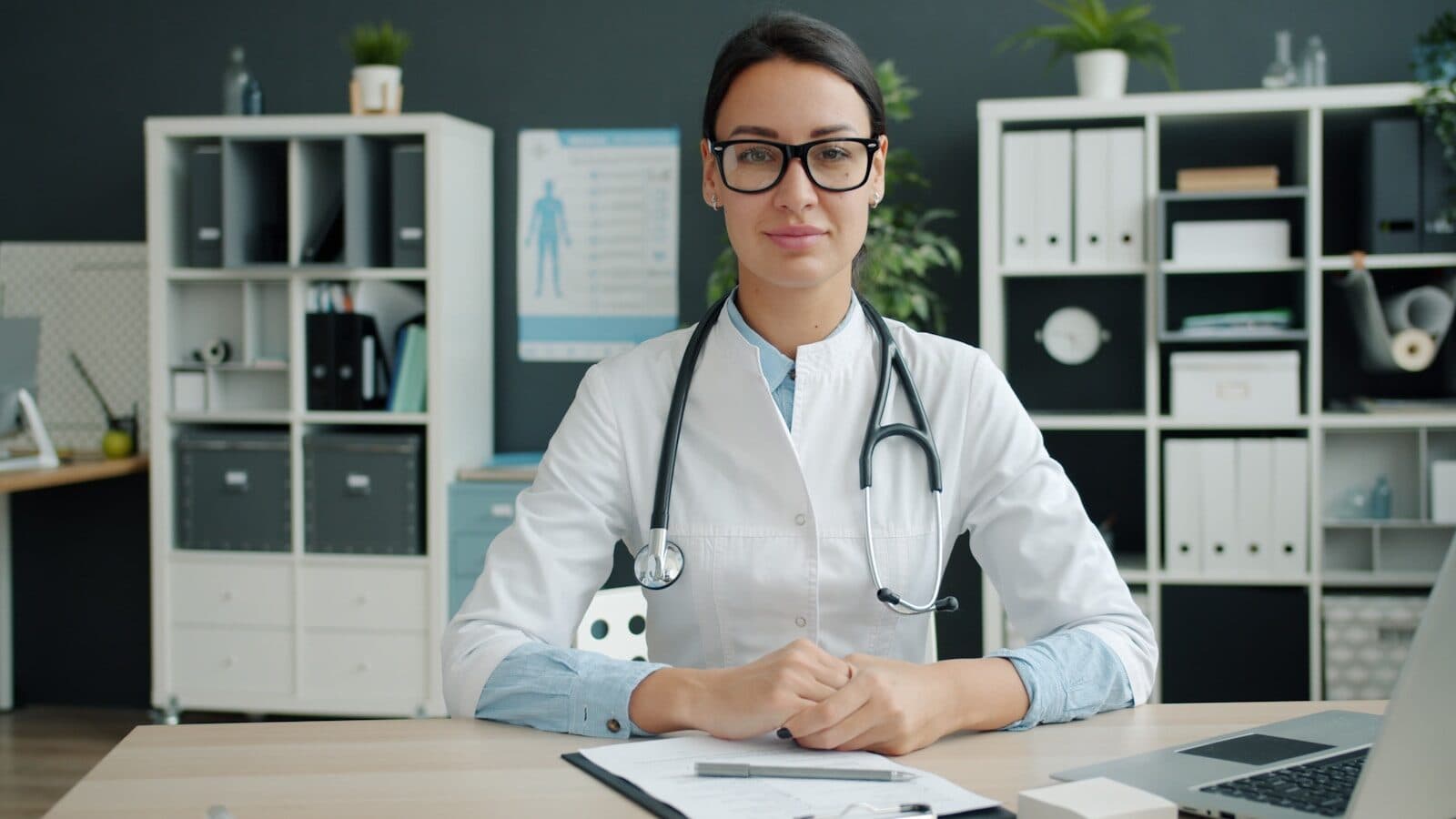 A female doctor wearing a stethoscope sits at her desk.